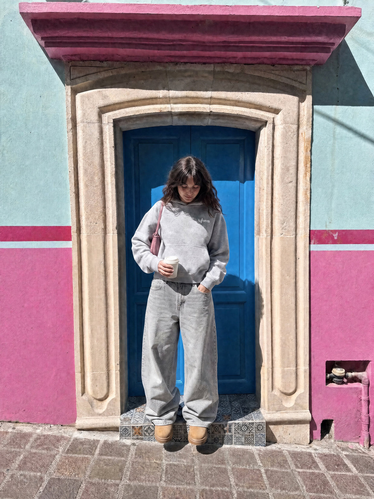 Marque de vêtement indépendante : hoodie LOVE U LUMIS gris chiné porté de face devant une maison rose et bleue
